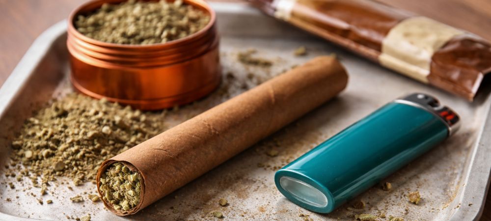 blunt de marihuana junto a grinder y mechero
