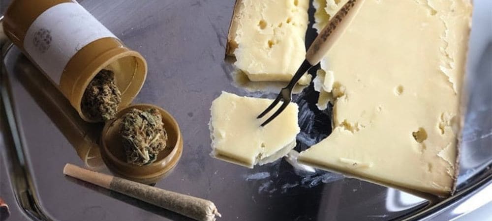 marihuana dentro de un bote, junto a un porro y acompañado en la misma bandeja de una cuña de queso rota por un tenedor de queso